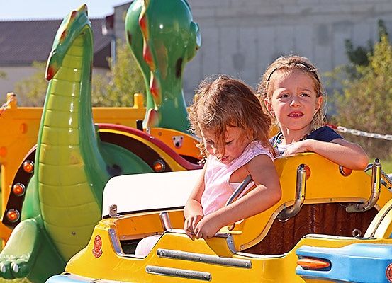 Zwei kleine Mädchen fahren eine gelbe und grüne Achterbahn mit grünem Drachendesign auf der Seite in einem Vergnügungspark.