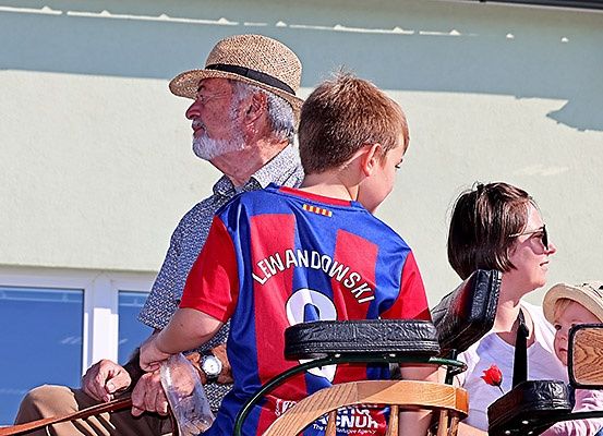 Ein älterer Mann und ein Junge in einem Lewandowski-Trikot sitzen auf einer Kutsche mit einer Frau und einem Baby, alle schauen nach vorne.