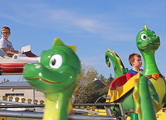 Zwei junge Jungen genießen eine Fahrt auf einer grün gefärbten Drachen-Attraktion im Vergnügungspark unter einem klaren blauen Himmel.