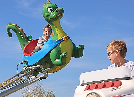 Zwei junge Jungen genießen eine Fahrt auf einer grünen, drachenförmigen Achterbahn unter blauem Himmel.