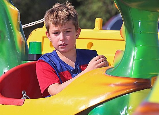 Ein junger Junge sitzt in einer Achterbahn in einem Vergnügungspark, sieht etwas besorgt aus und trägt eine blaue Weste.