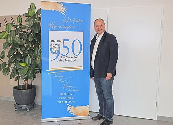 Ein Mann steht neben einem blauen Banner, das das 50-jährige Jubiläum von Novo Selo, Neudorf feiert.