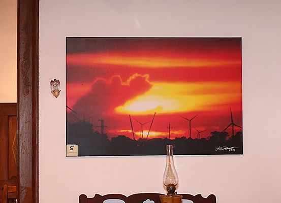 Ein gerahmtes Bild mit einem Sonnenuntergang, Windturbinen und einer alten Lampe auf einem Holztisch.
