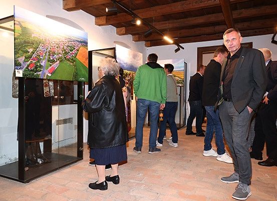 Mehrere Menschen stehen in einer Kunstgalerie und betrachten ausgestellte Gemälde. Eine Frau mit weißen Haaren schaut ein Gemälde in einem Glaskasten an.