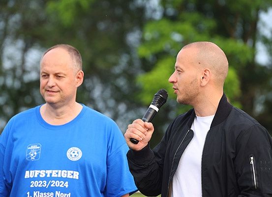 Ein Mann mit Mikrofon interviewt einen anderen Mann in einem blauen T-Shirt mit der Aufschrift Aufsteiger 2023/2024.