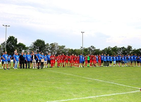 Eine große Gruppe von Fußballspielern in blauen und roten Trikots steht auf einem Feld, wobei zwei Personen Trophäen halten.