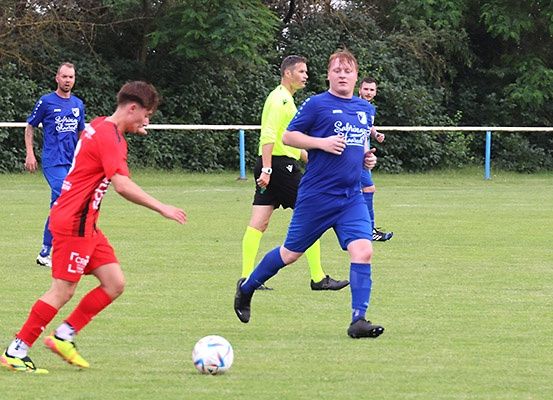 Ein Fußballspiel im Gange auf einem Feld, bei dem ein Spieler in Rot den Ball tritt, während andere in Blau und Gelb folgen.