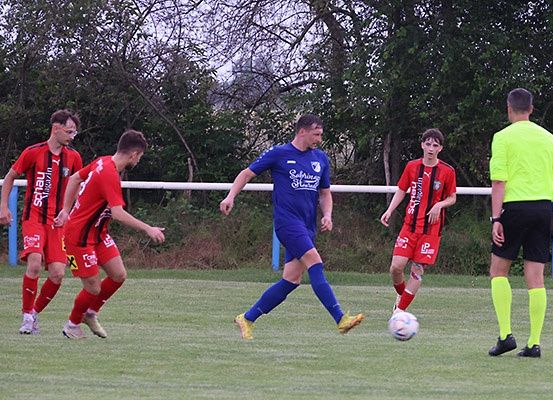 Fünf Fußballspieler auf einem Feld, zwei in Rot und einer in Blau, mit einem Schiedsrichter in Neongrün in der Nähe der Seitenlinie.