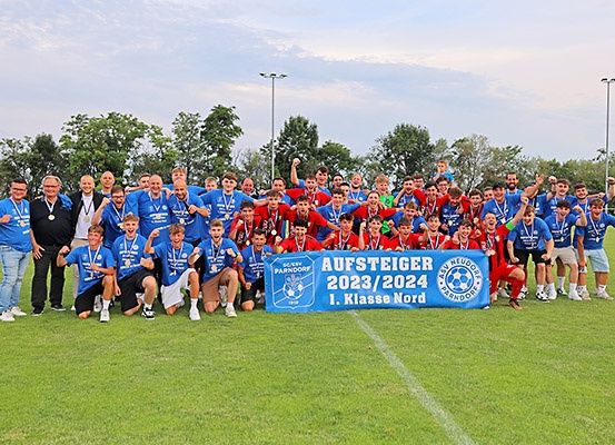 Eine Gruppe von Fußballspielern in blauen Trikots feiert einen Sieg auf einem Feld mit einem blauen Banner, das Aufsteiger 2023/2024 besagt.