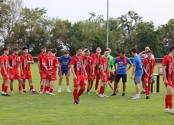 Eine Gruppe von Fußballspielern in roten Uniformen steht auf einem Feld, einige sind gebeugt, während andere hinter ihnen stehen, wahrscheinlich in einer Trainingseinheit.