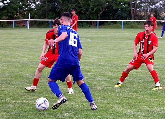 Ein Fußballspiel im Gange mit Spielern in blauen und roten Trikots, einer steht kurz davor, den Ball zu schießen.