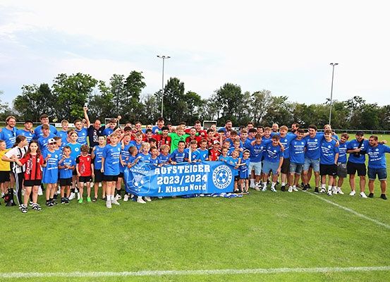 Eine Fußballmannschaft posiert für ein Gruppenfoto auf dem Feld mit einem blauen Banner, das Aufsteiger 2023/2024 1. Klasse Nord besagt.