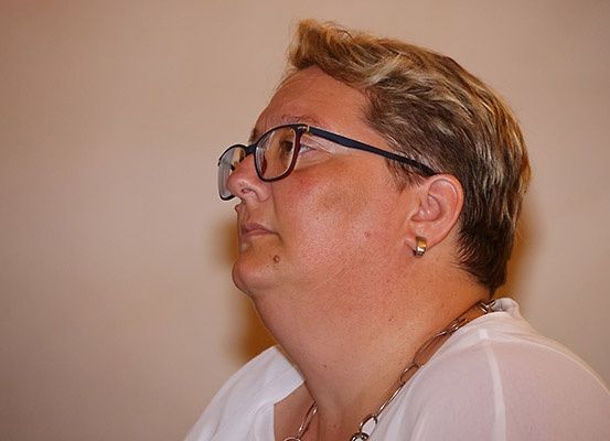 Eine Frau mit kurzen Haaren trägt eine Brille und eine Halskette. Sie schaut nach oben.