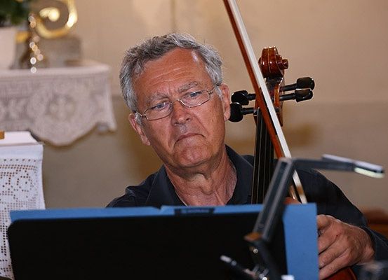 Ein älterer Mann mit Brille spielt eine Geige und schaut auf das Notenpult, mit einem weißen Tuch im Hintergrund.