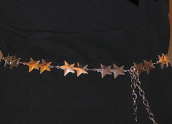 Ein schwarzes Kleid mit einem Gürtel, der mit goldenen Sternen und silbernen Ketten verziert ist, flach auf einer Oberfläche liegend.