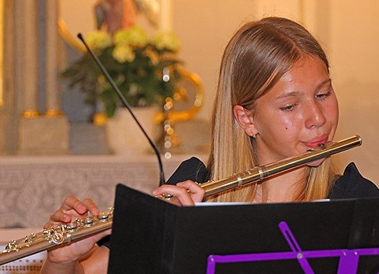 Ein junges Mädchen spielt eine Flöte in einer Kirche. Sie ist konzentriert und hält die Flöte dicht vor ihr Gesicht. Ein Mikrofon steht vor ihr.