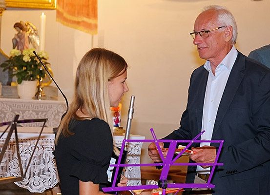 Ein älterer Mann reicht einer jungen Frau eine Flöte, während sie in einer Kirche stehen.
