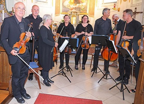 Eine Gruppe von Musikern, darunter Geiger, steht mit ihren Instrumenten in einer Kirche, bereit zum Auftritt.