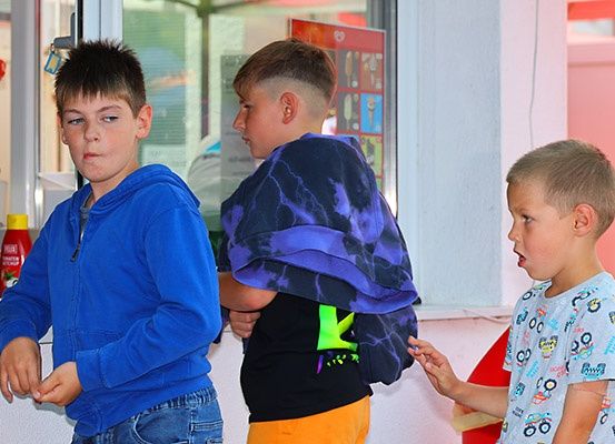 Drei Jungen stehen in einem Raum. Der Junge in der Mitte hat ein lila Färbehandtuch auf seiner Schulter. Der Junge rechts hält etwas in der Hand.