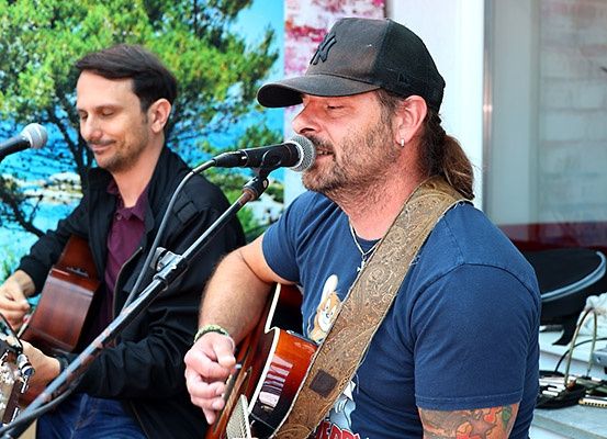 Zwei Männer treten auf der Bühne auf. Ein Mann spielt Gitarre und singt, während ein anderer Mann Gitarre spielt. Sie stehen beide vor einem Mikrofon.