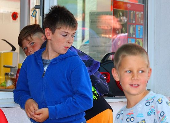 Drei Jungen stehen an einem Tresen in einem Restaurant, einer trägt eine blaue Kapuzenjacke, ein anderer eine lila Kapuzenjacke und ein Dritter ein weißes Shirt mit Design.