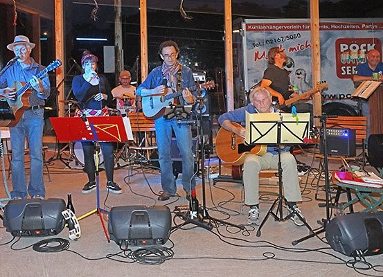 Eine Band spielt auf der Bühne mit Gitarren, Mikrofonen und Lautsprechern unter einem blauen Nachthimmel.