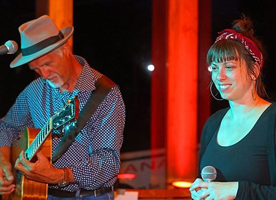 Ein Mann spielt Gitarre, während eine Frau in ein Mikrofon auf der Bühne singt.
