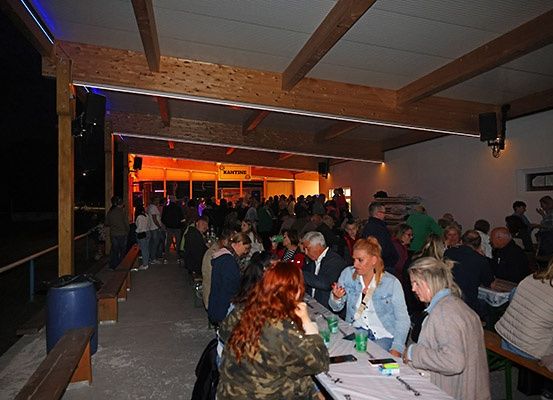 Eine Gruppe von Menschen versammelt sich nachts in einem Restaurant. Einige sitzen, andere stehen. Sie führen Gespräche.
