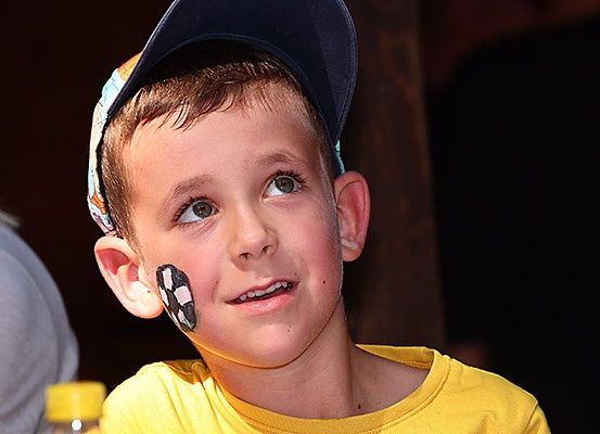 Ein junger Junge mit blauer Mütze und gelbem T-Shirt lächelt mit Gesichtsbemalung auf der Wange.