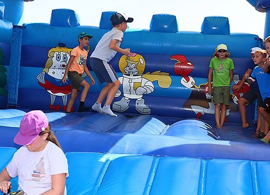 Kinder spielen auf einem blauen Aufblasbaren mit Cartoon-Charakteren, eines springt, während andere zusehen.