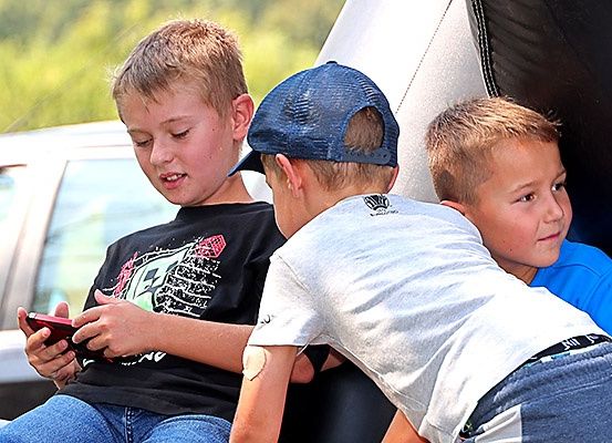 Drei Jungen sitzen zusammen, einer in einem schwarzen Shirt hält ein Handy, während die anderen beiden zusehen.