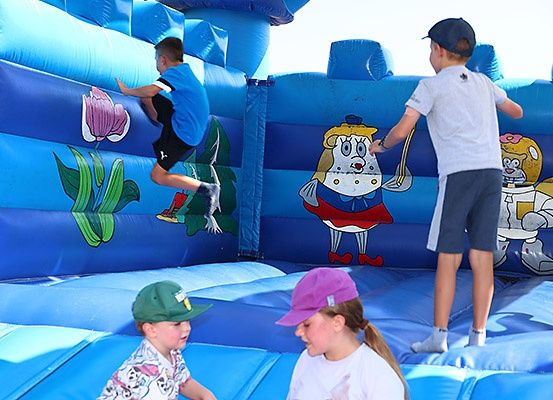 Vier Kinder spielen in einem blauen aufblasbaren Spielbereich. Zwei Kinder klettern, und zwei beobachten.