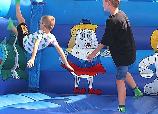Zwei Jungen spielen in einem blauen aufblasbaren Spielbereich, einer trägt eine Brille und bunte Socken.