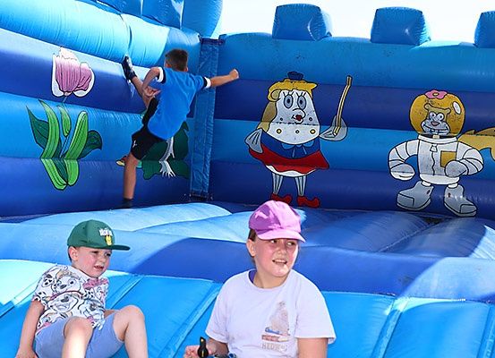 Drei Kinder spielen auf einem blauen aufblasbaren Spielgerät mit Cartoon-Charakteren. Ein Kind klettert, während die anderen sitzen.