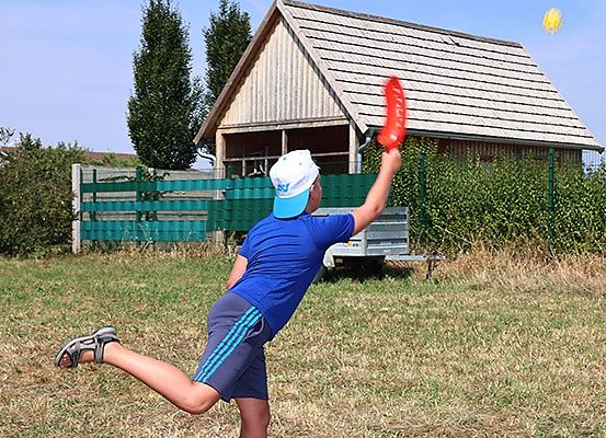 Ein junger Junge in einem blauen T-Shirt wirft einen Frisbee auf einem Rasen in der Nähe eines Holzhauses.