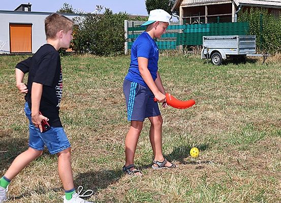 Zwei Jungen spielen mit einem Frisbee und einem Ball auf einem Grasfeld. Ein Junge jagt dem anderen nach, während er einen roten Frisbee hält.