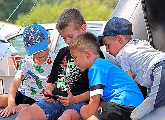 Vier Jungen sitzen auf der Stoßstange eines Autos, beschäftigt mit ihren Handys, während ein Junge seinen Kopf auf der Schulter eines anderen ruht.