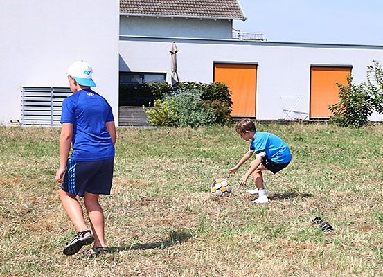 Ein Mann und ein Junge spielen Fußball im Garten eines Hauses. Der Junge ist dabei, den Ball zu schießen.