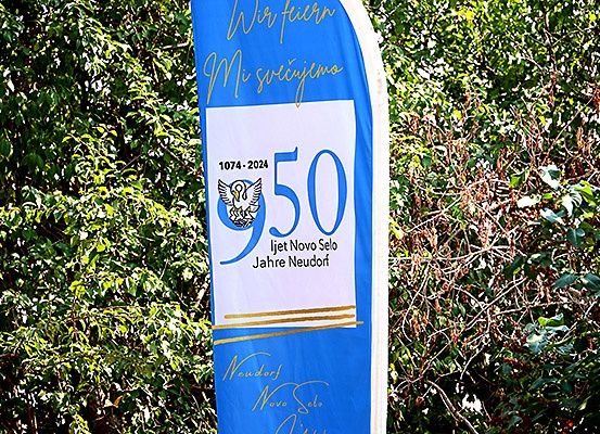 Ein blauer Banner mit weißen Text steht vor einem Busch. Es steht '950' und '1074-2024', vermutlich zur Erinnerung an einen 950. Jahrestag. Ein Adlerlogo ist vorhanden.