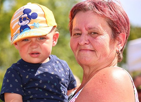 Eine ältere Frau hält einen kleinen Jungen, der eine Mickey-Mouse-Mütze und ein blaues T-Shirt mit kleinen Mustern trägt.