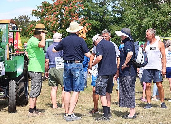 Eine Gruppe von Menschen steht um einen grünen Traktor auf einem Rasenfeld, möglicherweise bei einer Veranstaltung im Freien.