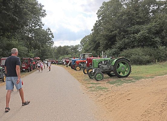 Ein Mann geht einen Weg entlang, an dem Oldtimer-Traktoren geparkt sind. In der Nähe versammeln sich Menschen um die Traktoren.