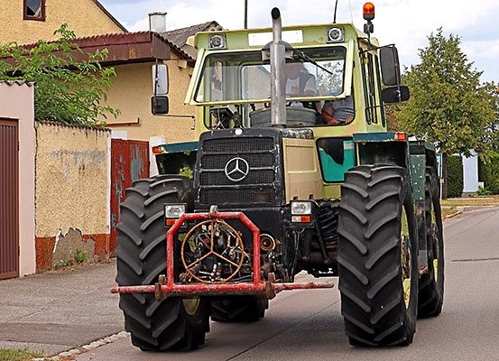 Ein großer, gelber und grüner Mercedes Traktor fährt eine Straße entlang in der Nähe eines Gebäudes mit einer braunen Tür.