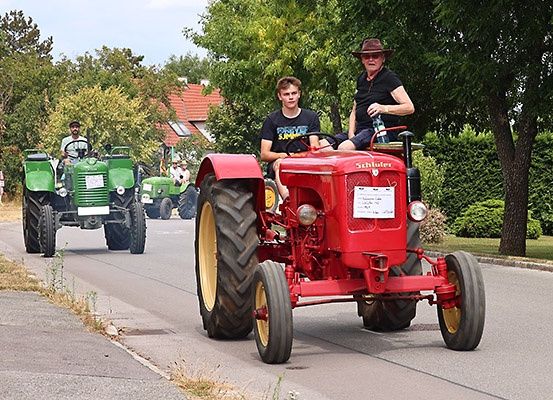 Drei Traktoren fahren auf einer Straße, wobei eine Person mit einer Flasche auf dem Vordersitz eines der Traktoren sitzt.