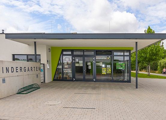 Das Äußere eines Kindergartens mit einer grünen Wand und Glastüren, einem Ziegelpflaster und einem bewölkten Himmel.