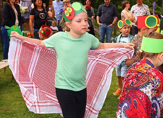 Eine Gruppe von Kindern in Kostümen führt ein Theaterstück in einem Park auf, während eine Menge Erwachsener zuschaut.
