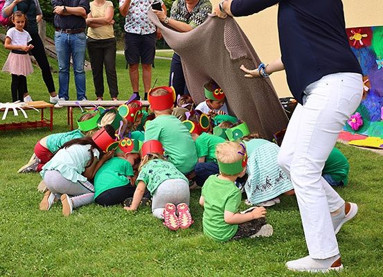 Eine Gruppe von Kindern in grünen Hemden und Stirnbändern sitzt auf einem Grasfeld, während Erwachsene im Hintergrund zusehen.