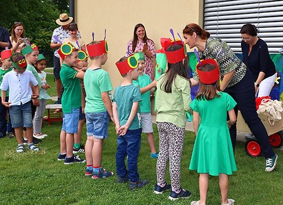 Kinder in grünen Hemden und Marienkäfer-Hüten führen ein Theaterstück auf dem Rasen auf. Eine erwachsene Frau hilft ihnen.
