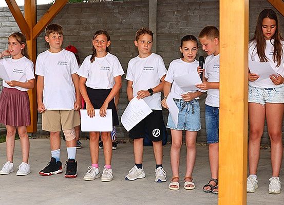 Eine Gruppe von Kindern in identischen weißen T-Shirts steht zusammen und hält Papiere in der Hand, möglicherweise nehmen sie an einer Schulveranstaltung teil.