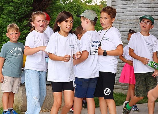 Eine Gruppe von Kindern in weißen T-Shirts steht draußen an einem sonnigen Tag. Ein Kind trägt ein graues T-Shirt.